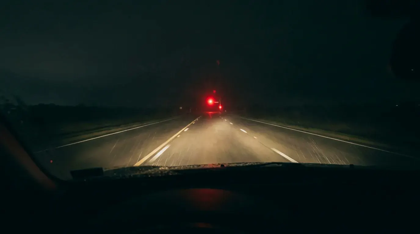 An empty highway at night through a rainy windshield, one red signal ahead