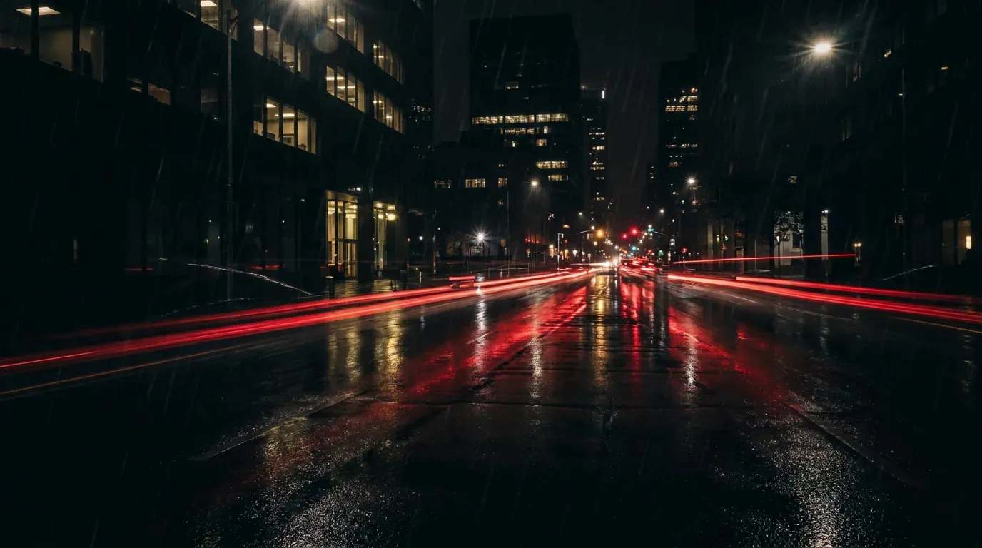 A wet city street at night with red tail lights reflected