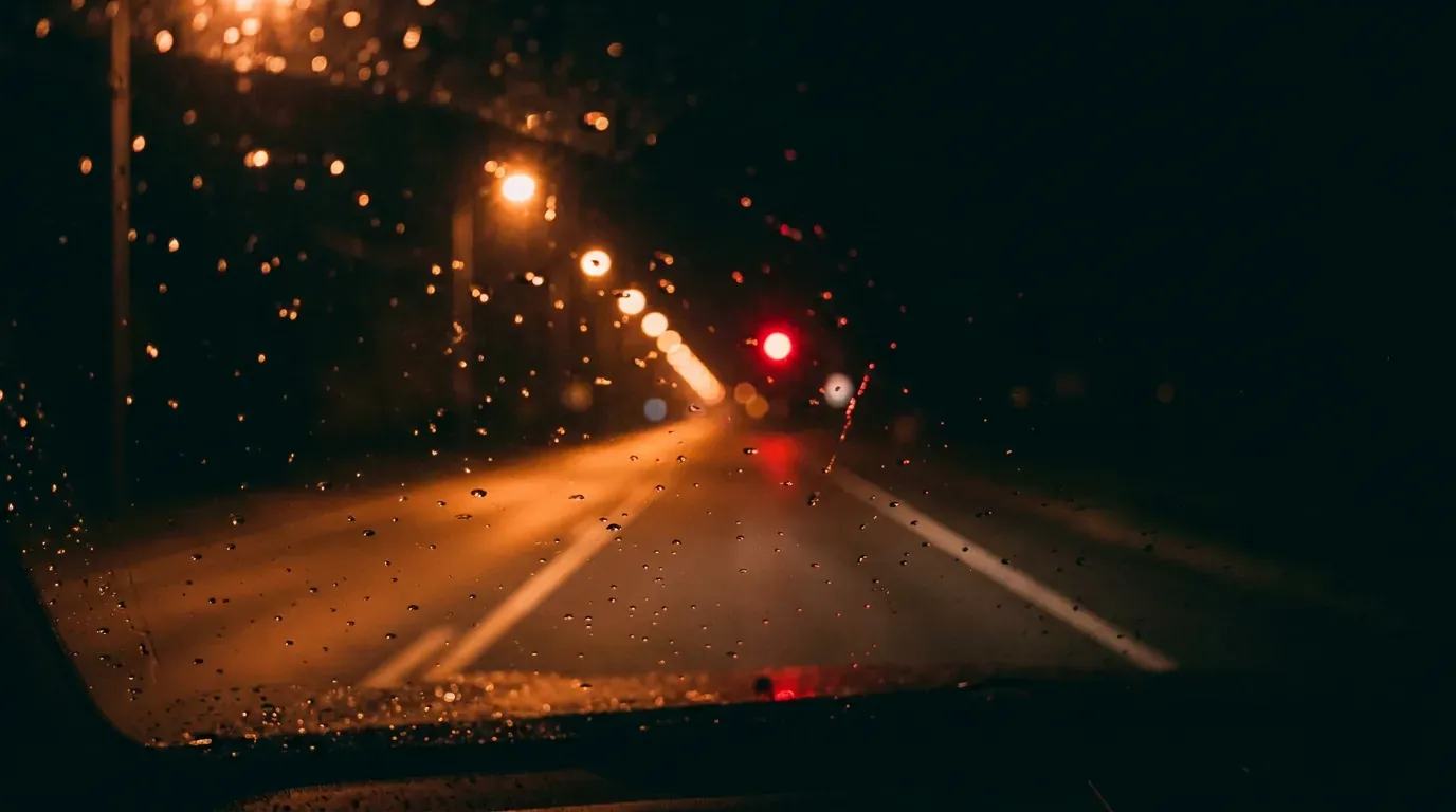 Rain on a windshield at night with the empty road lit by streetlights